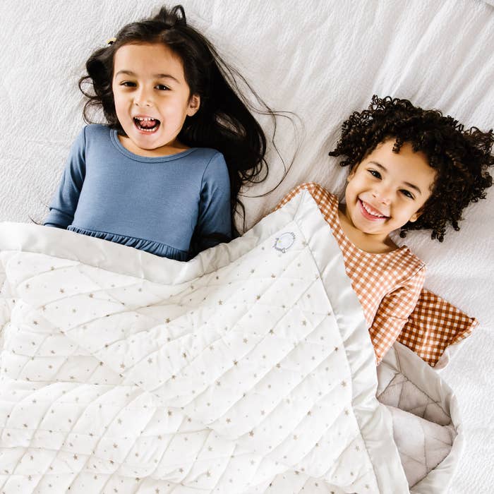 Two children under quilted white blanket with star designs