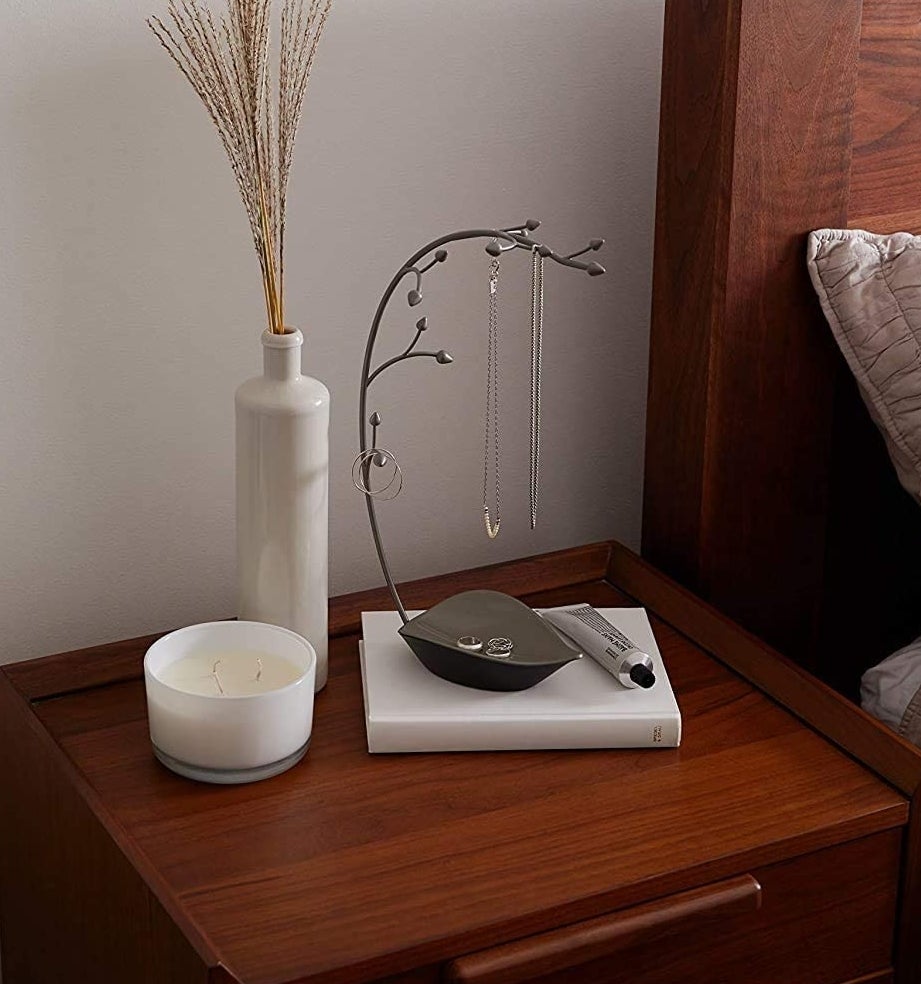 The filled jewellery holder on a nightstand beside a vase and a candle