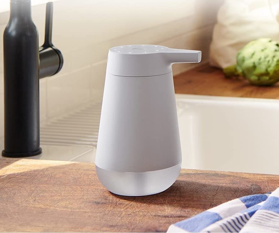 The white smart soap dispenser on a kitchen counter next to the sink