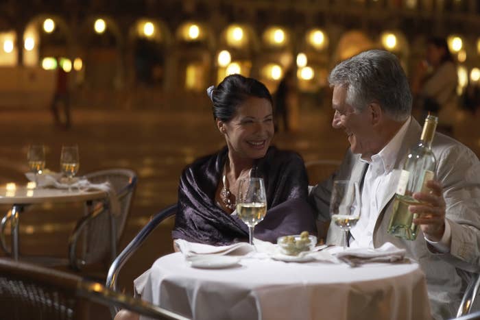 A wealthy couple sitting at a restaurant table outside enjoying a bottle of white wine