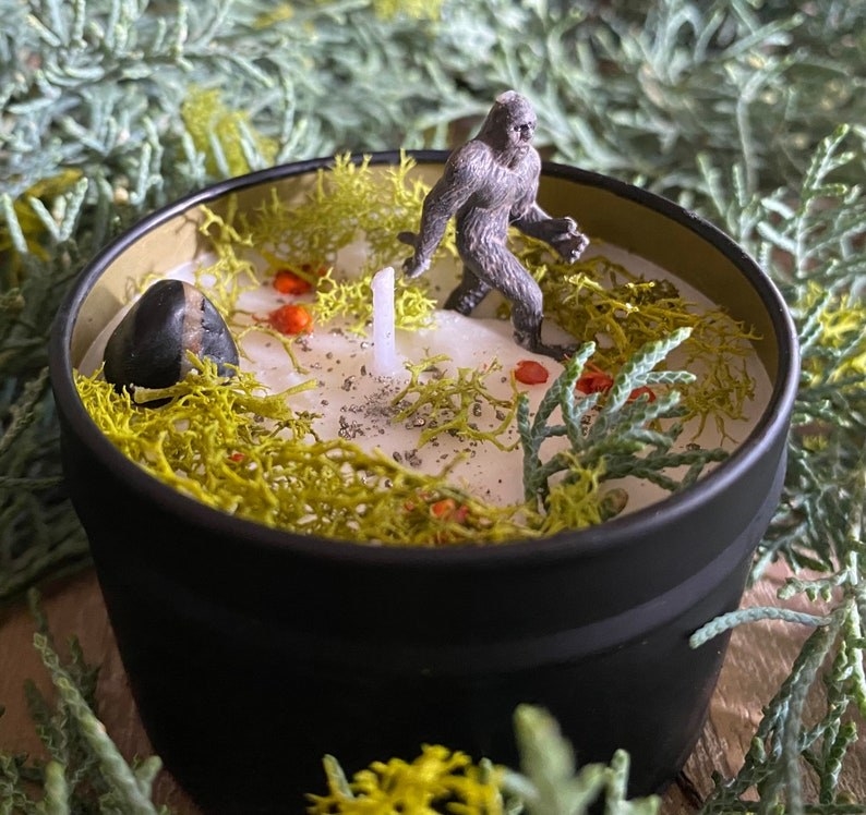 a candle with a mini Sasquatch figurine and nature elements on top of the wax