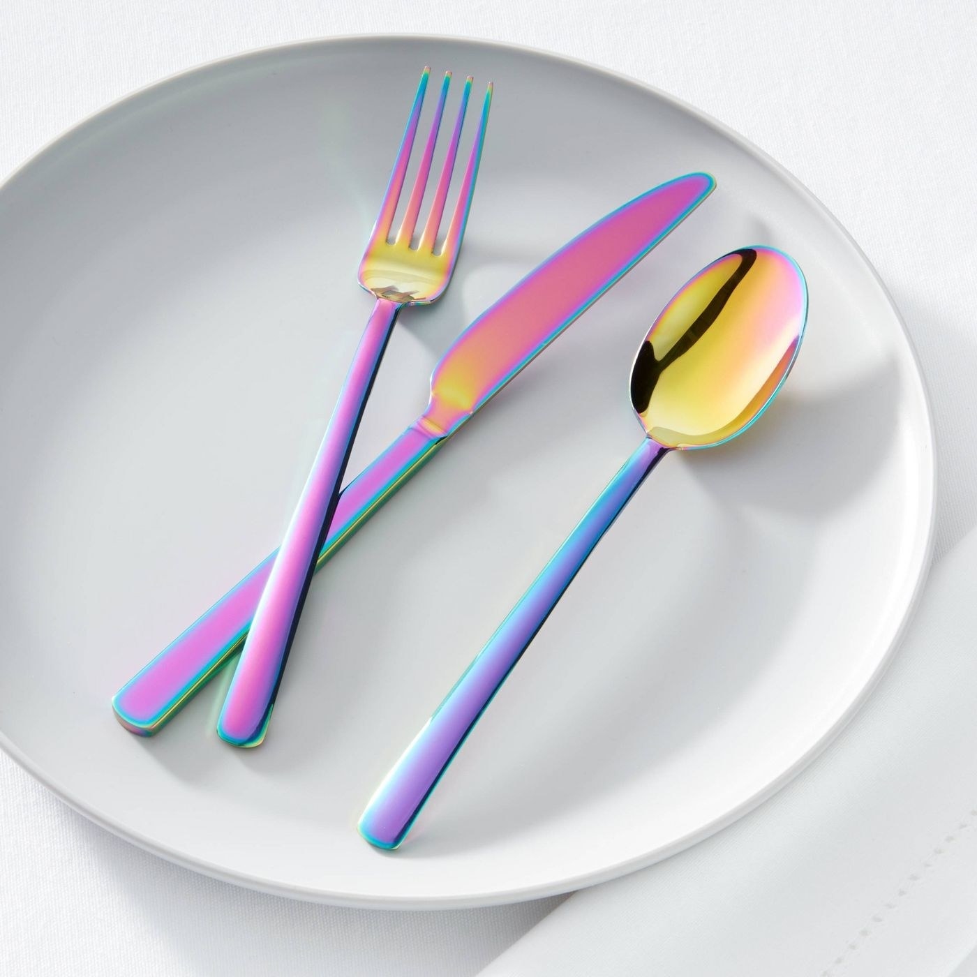 A fork, knife and spoon in an iridescent finish sitting on a white plate
