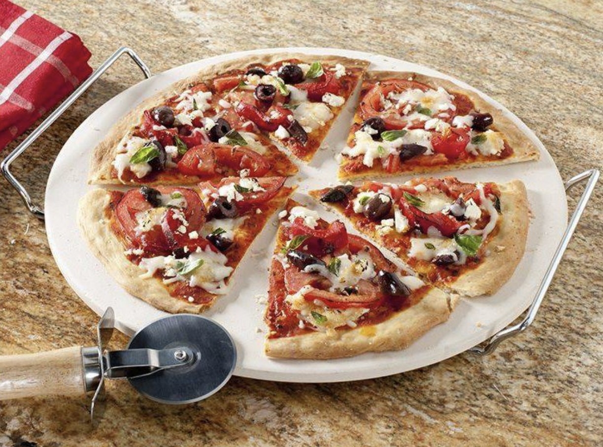 Pizza with olives and tomatoes on a pizza slab next to a pizza cutter