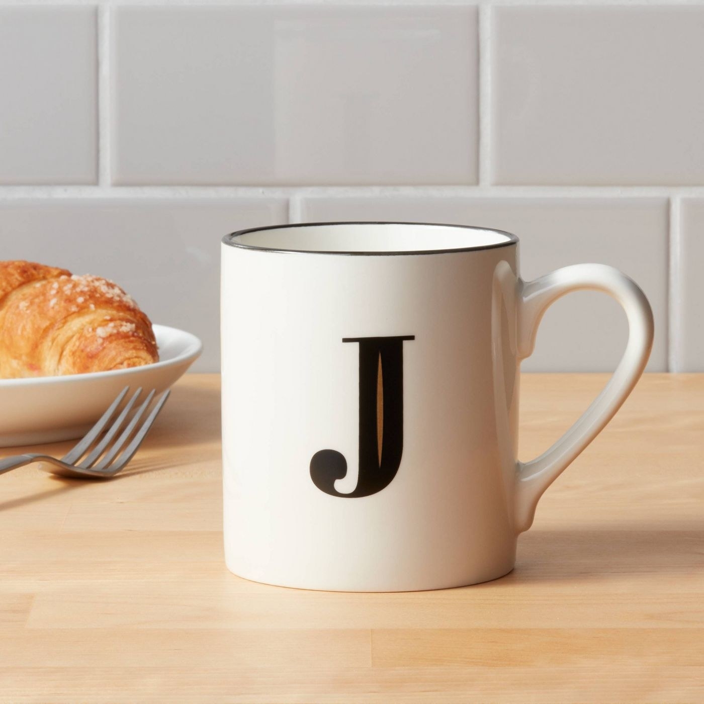 A white mug with a &quot;J&quot; initial in black and gold sitting on a kitchen countertop