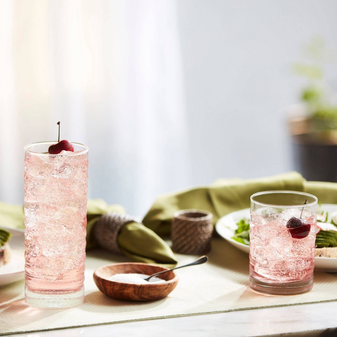 Two textured glasses with a fizzy drink and cherries