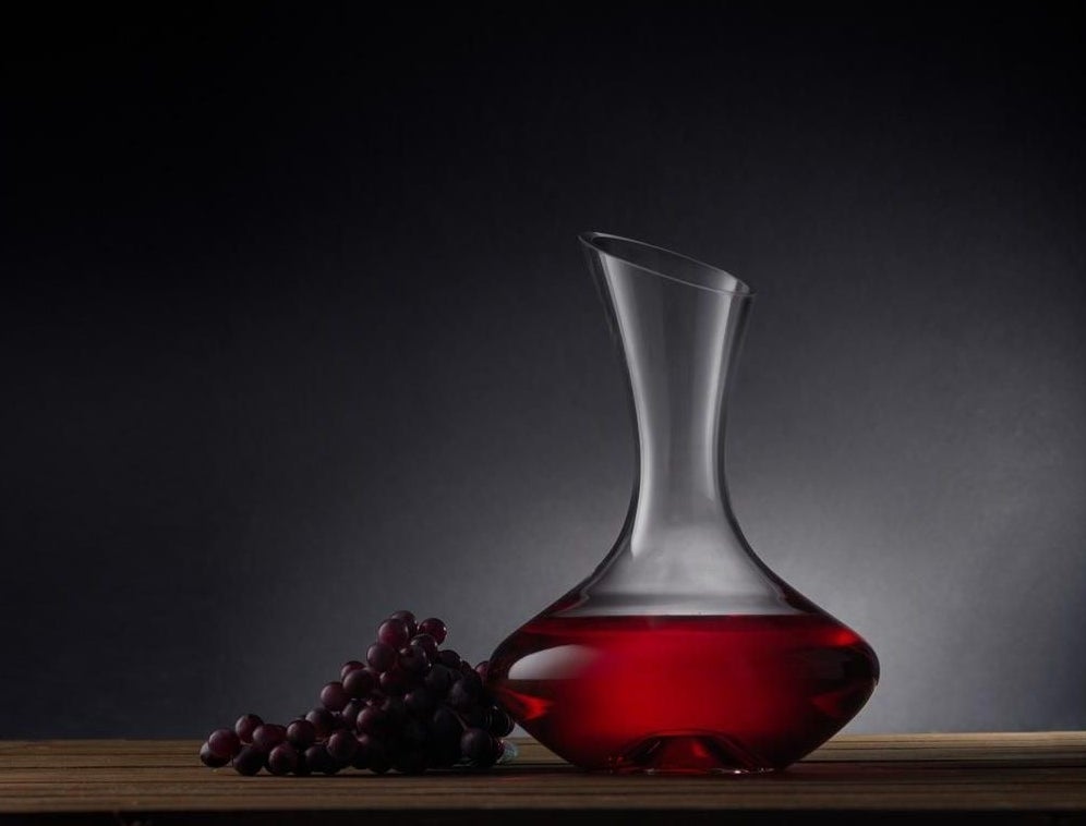 A decanter filled with red wine, sitting on a table next to red grapes