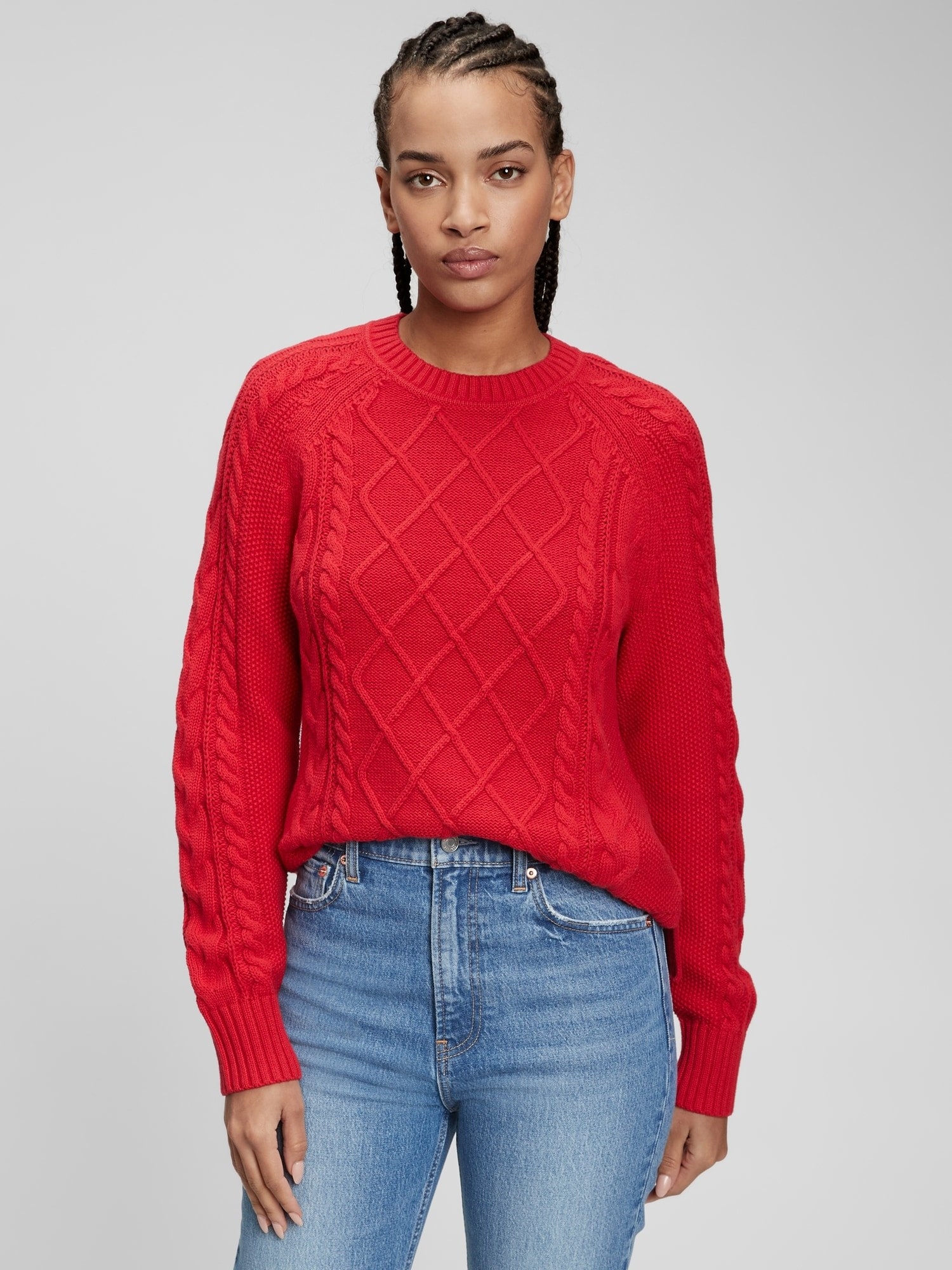model wearing a red cable knit sweater with light blue jeans