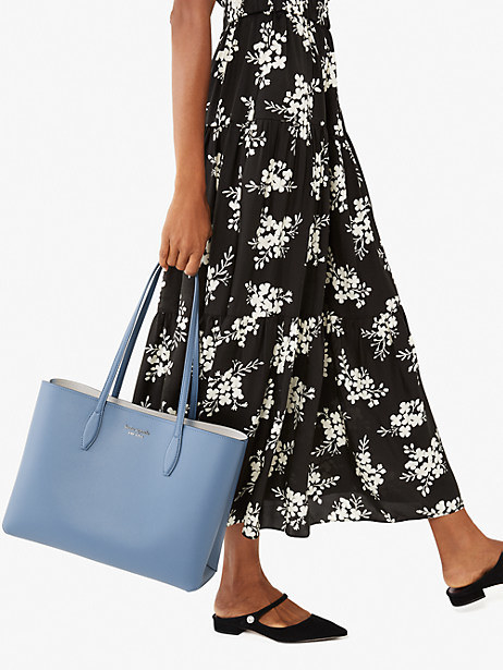 Model carrying blue leather tote bag by the handles