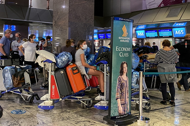 People with suitcases and wearing masks in a close line up at an airport terminal