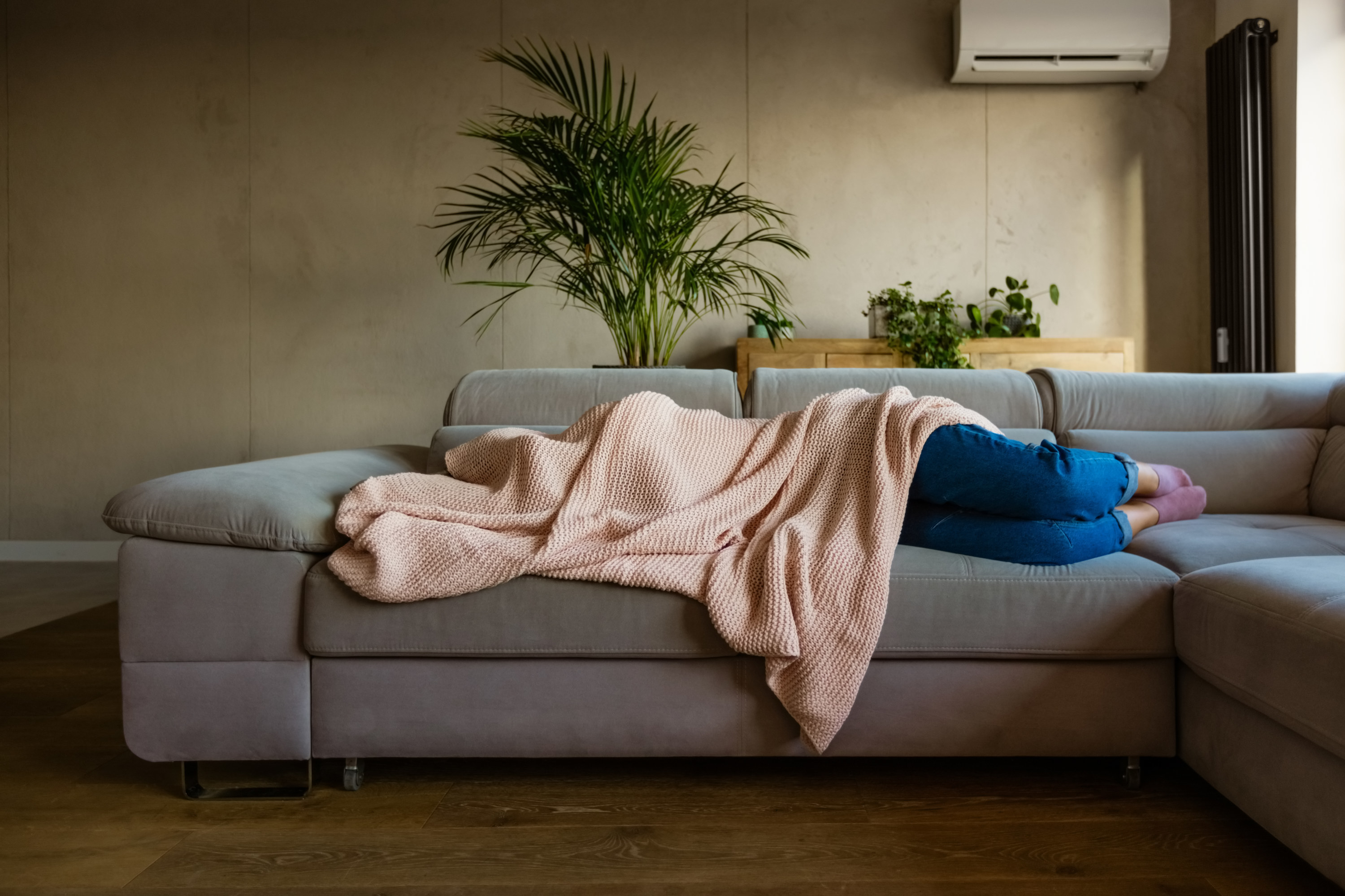 A person lying on a couch under a blanket with just their legs sticking out