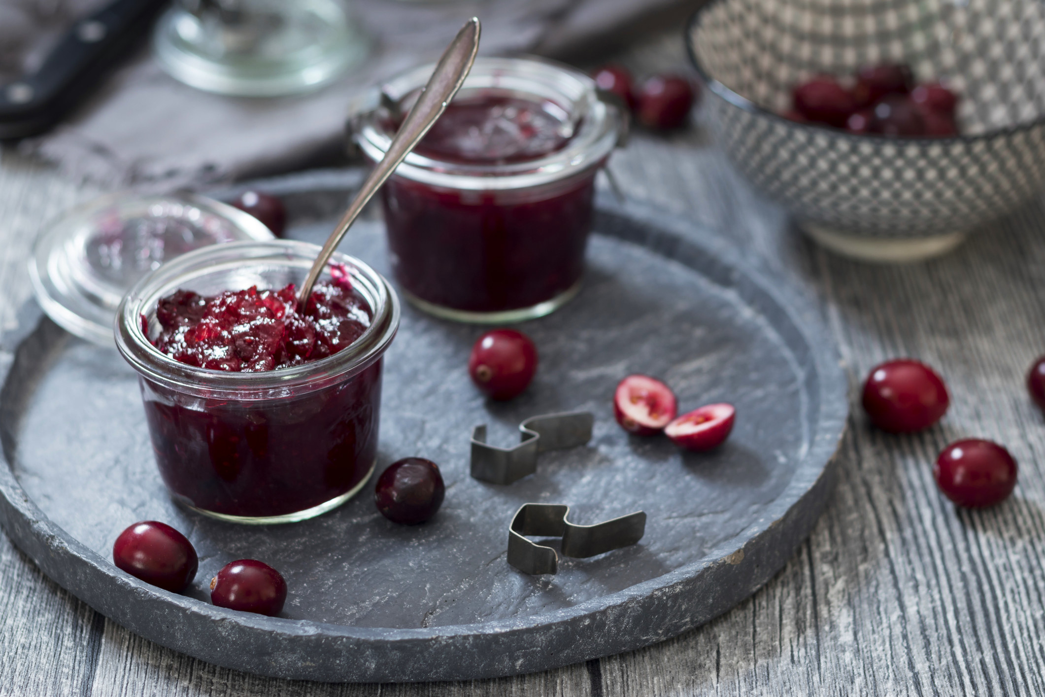Two pots of cranberry sauce sitting on a slate plate, surrounded by whole cranberries.