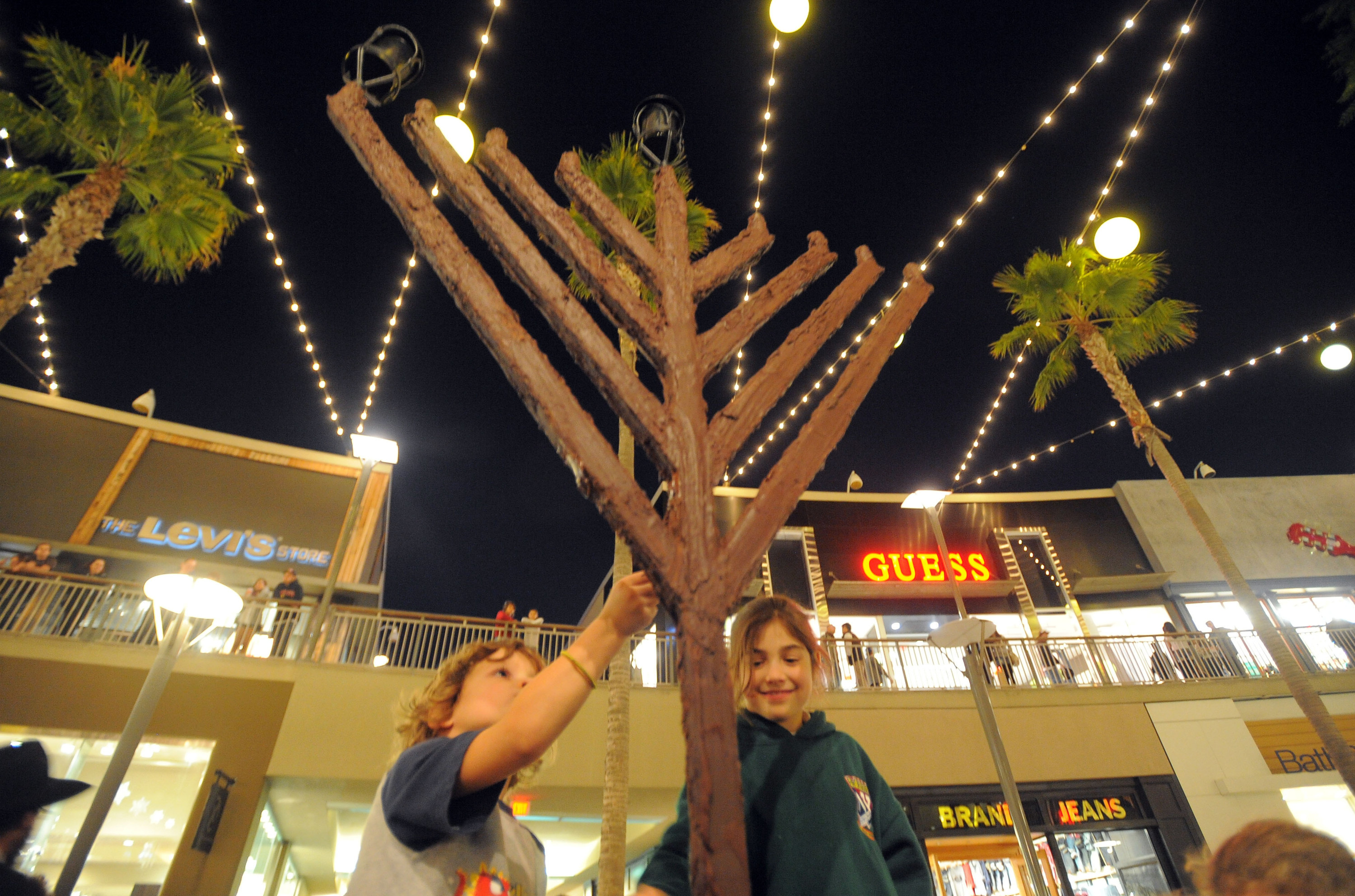 A menorah made of chocolate with two children below it, stores in the background