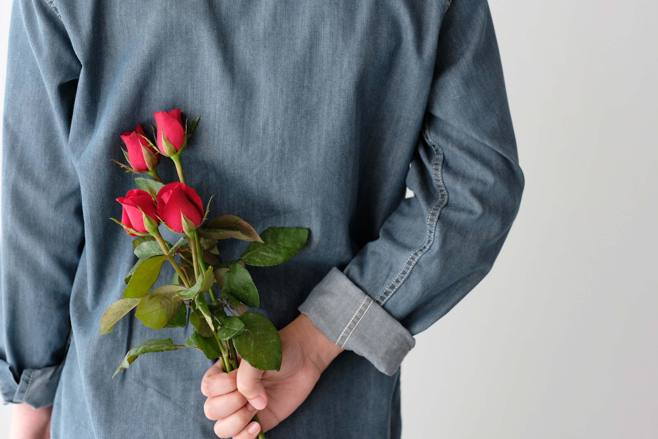 Someone holds roses for a date behind their back