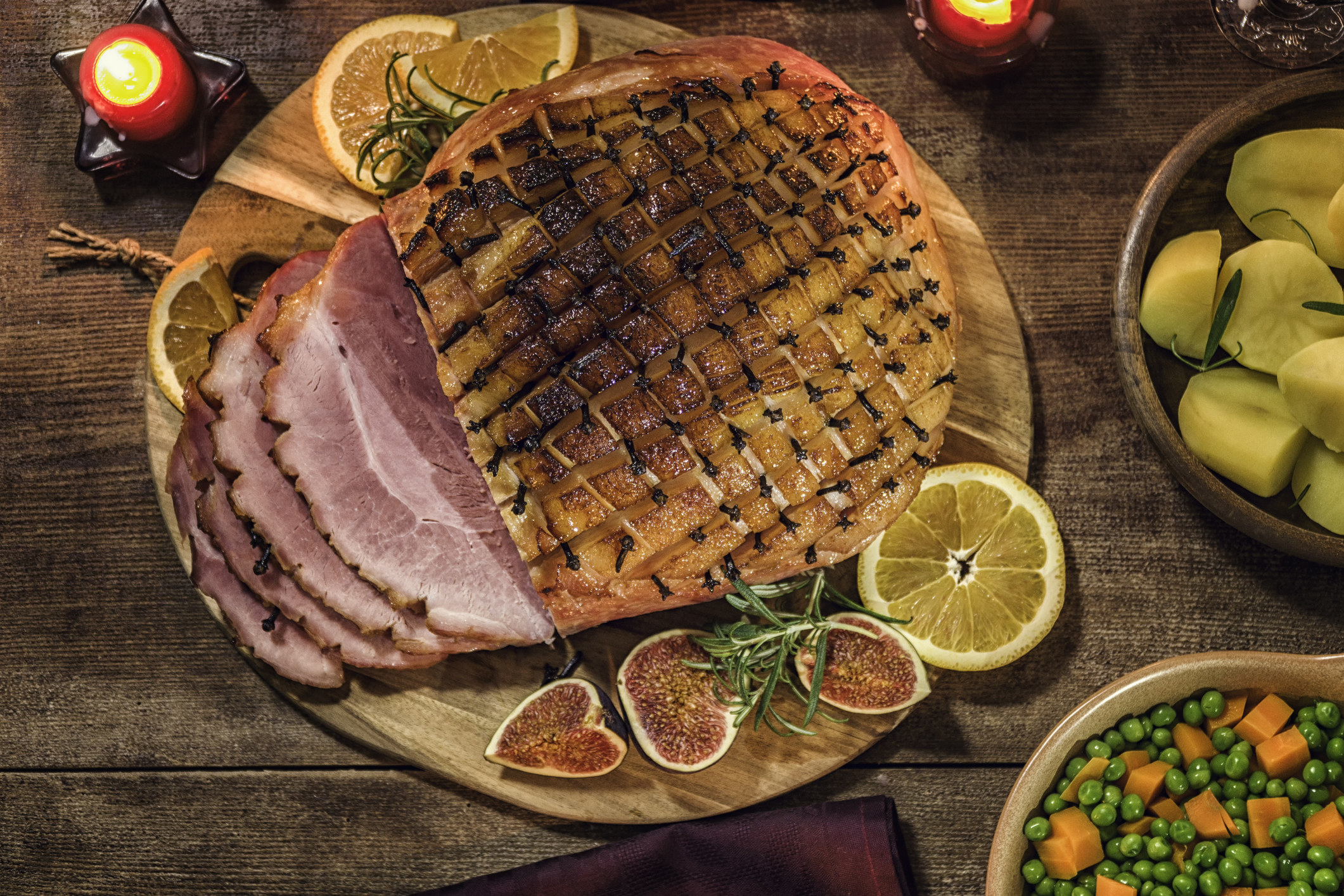A ham joint with some slices, sitting on a chopping board and surrounded by cut up fruit.