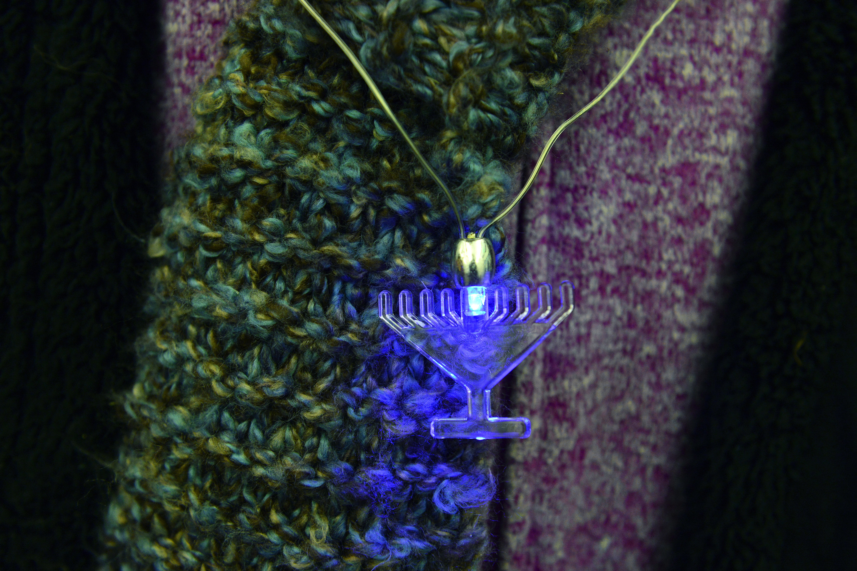 A menorah necklace glows against a persons scarf