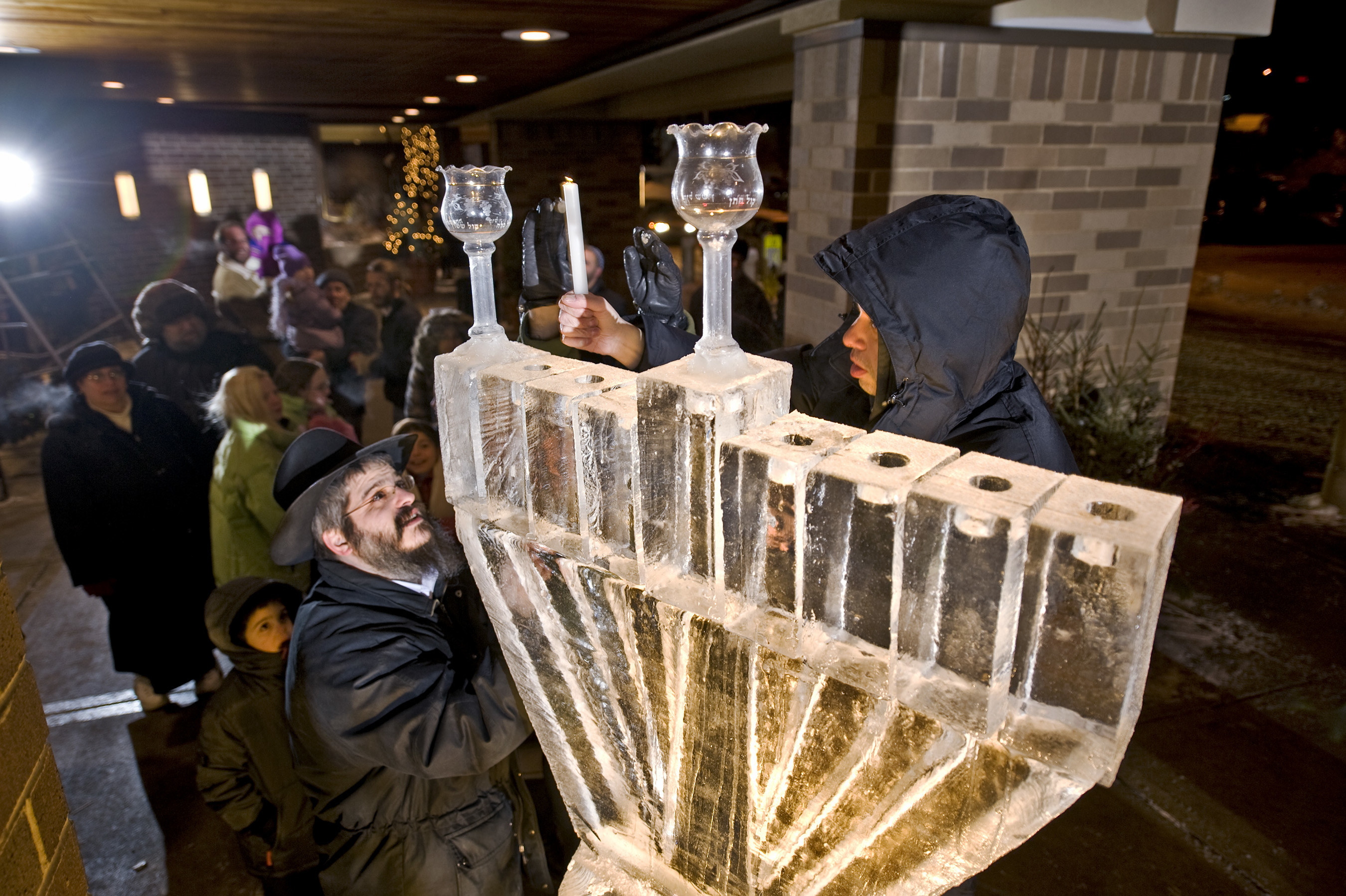 Two men light a menorah made of ice in front of a crowd