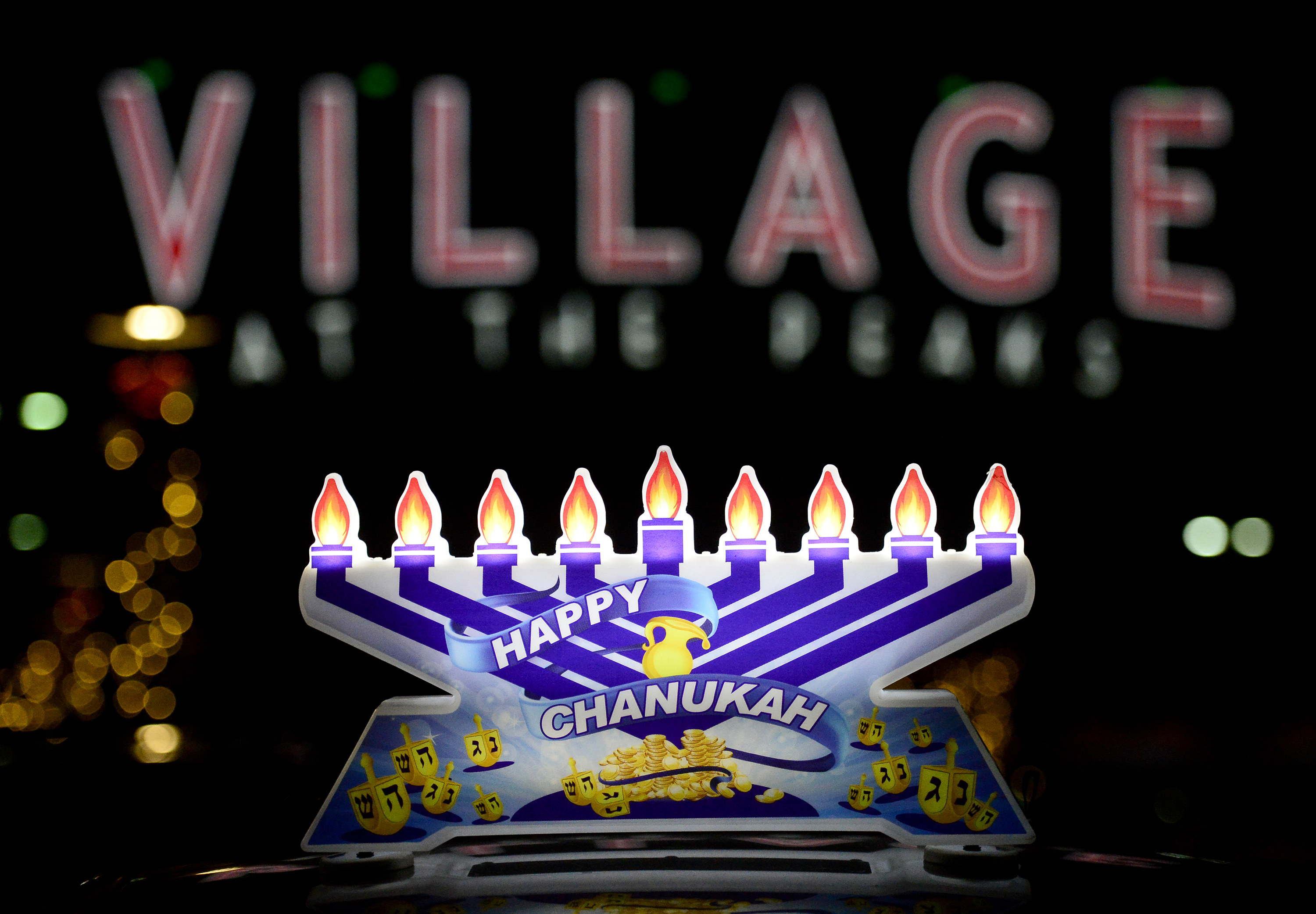 A menorah decoration reads &quot;happy chanukah,&quot; behind it you can see a large sign that reads &quot;Village&quot;