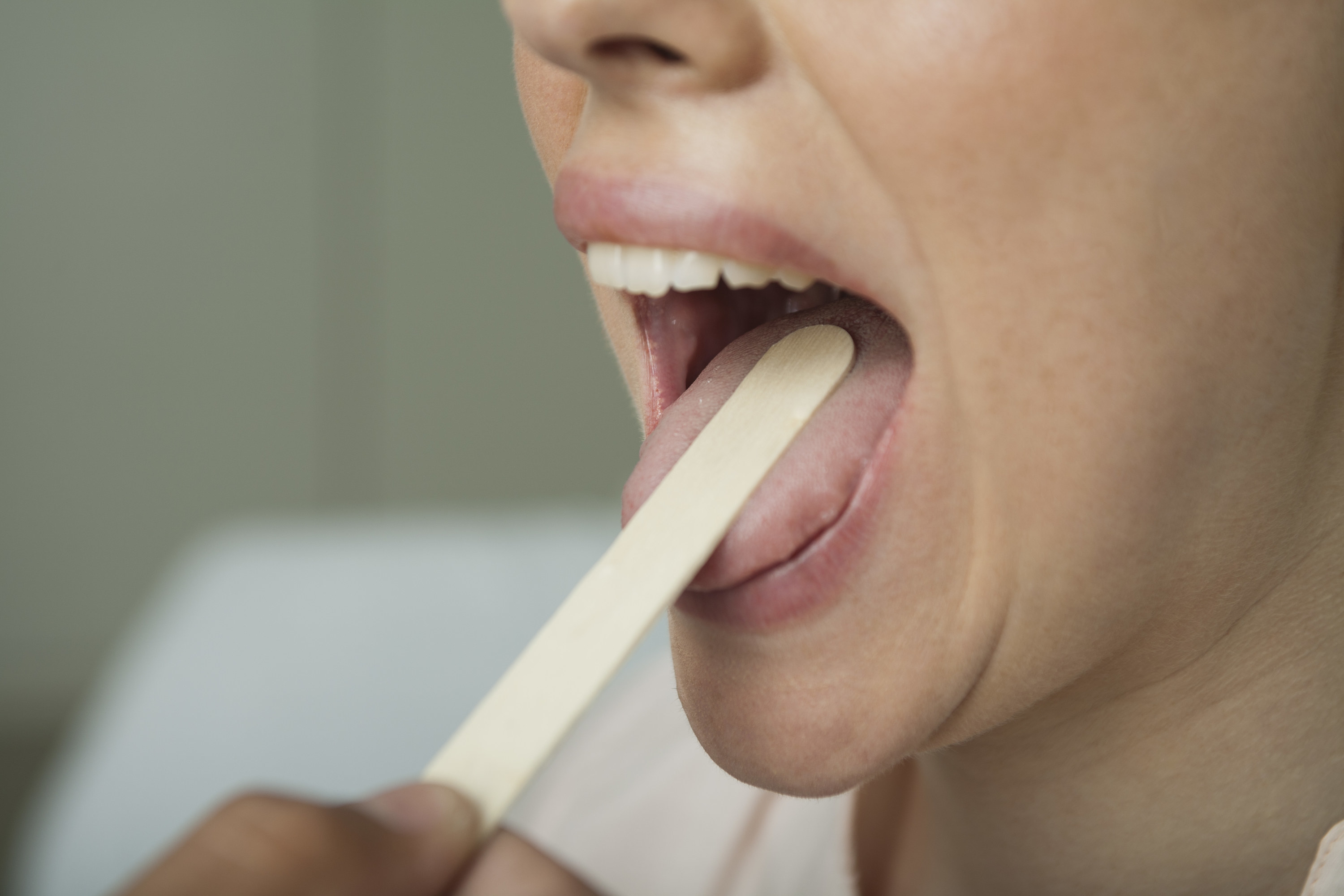 woman with her mouth open as the doctor uses a tongue depressor to check her throat