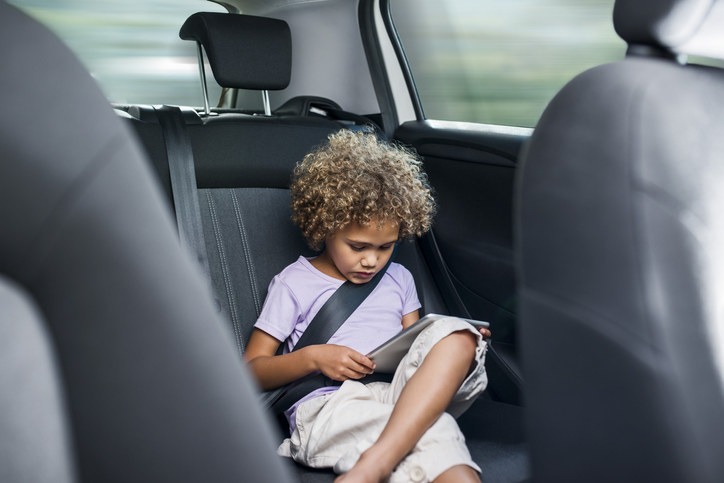 Little girl using digital tablet while sitting on car&#x27;s back seat