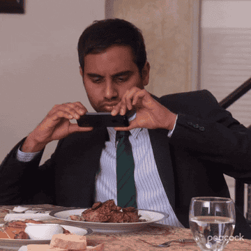 Aziz Ansari as Tom Haverford taking a photo of his plate of food