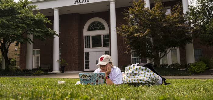 A girl sitting in the lawn on her stomach working on her laptop next to her backpack