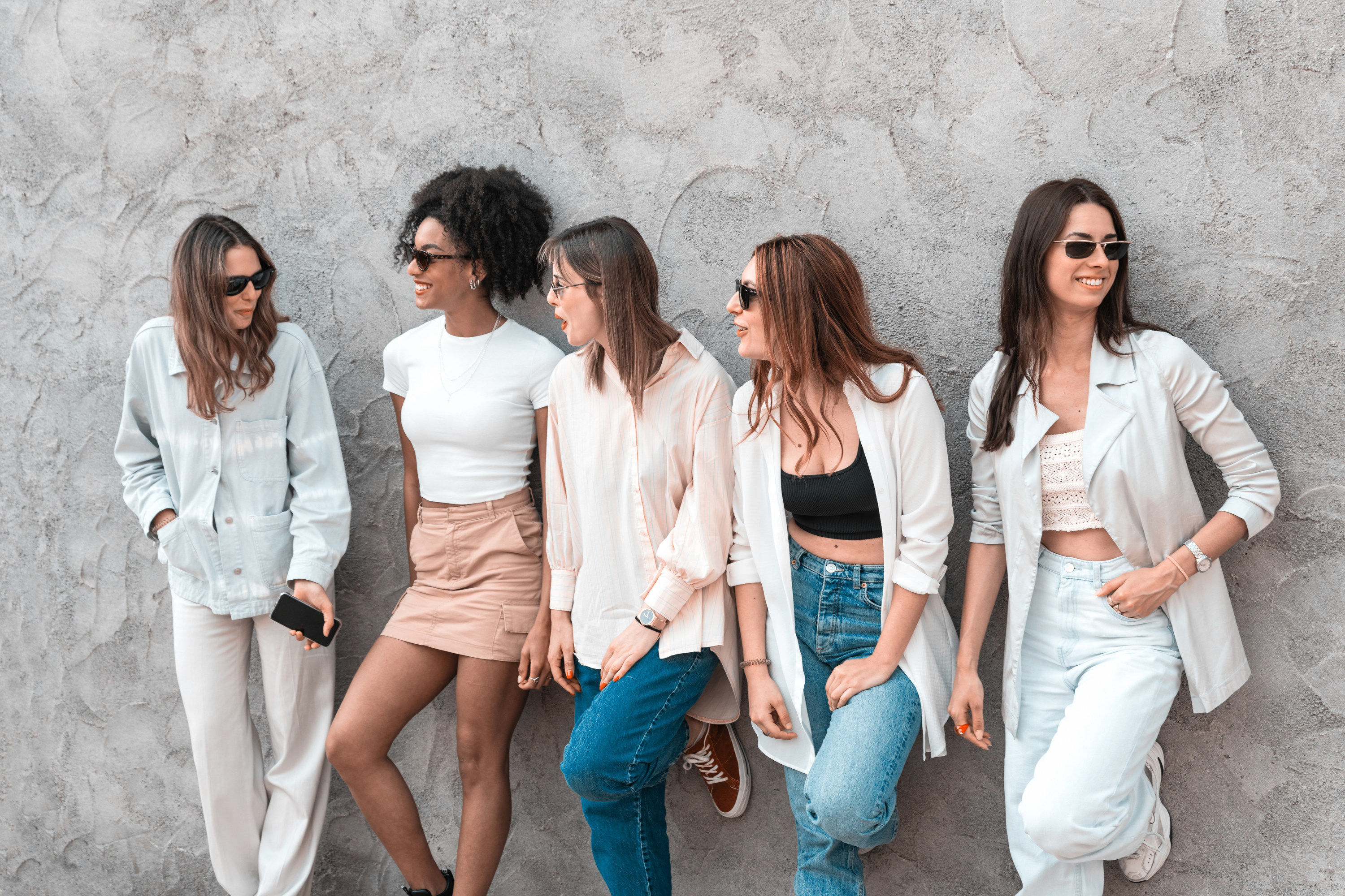 A group of five girls leaning against a wall talking