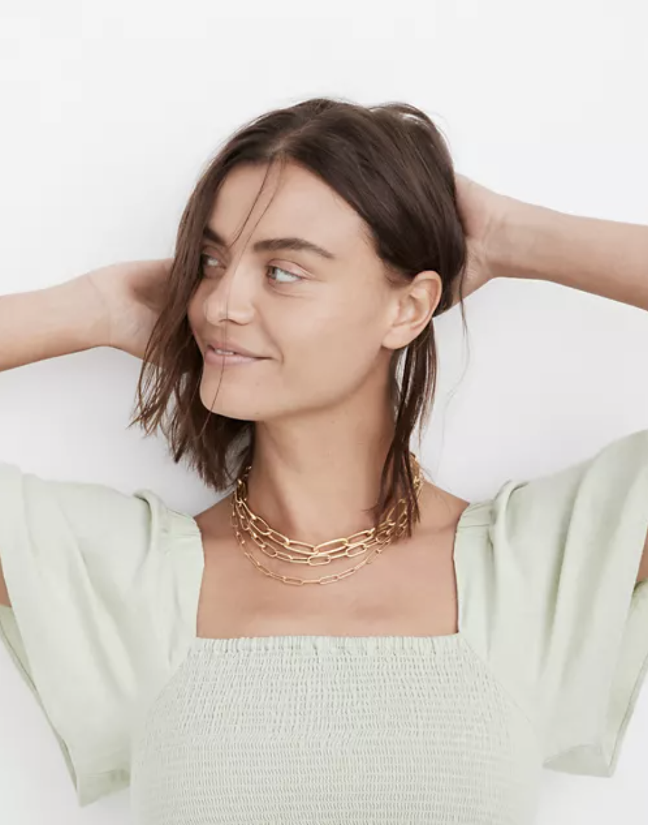 Model wearing three gold paperclip necklaces