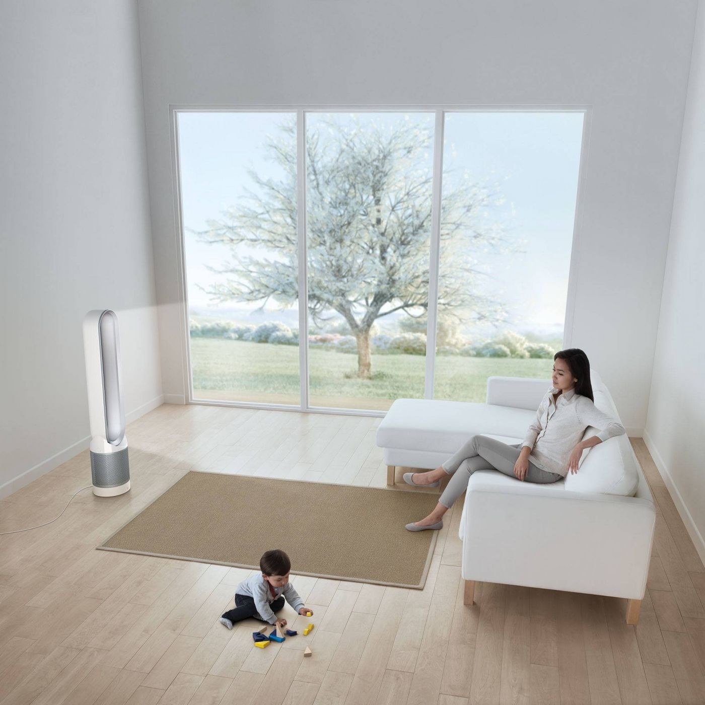 A woman sits on her couch watching a child play, which the Dyson fan oscillates in the room.