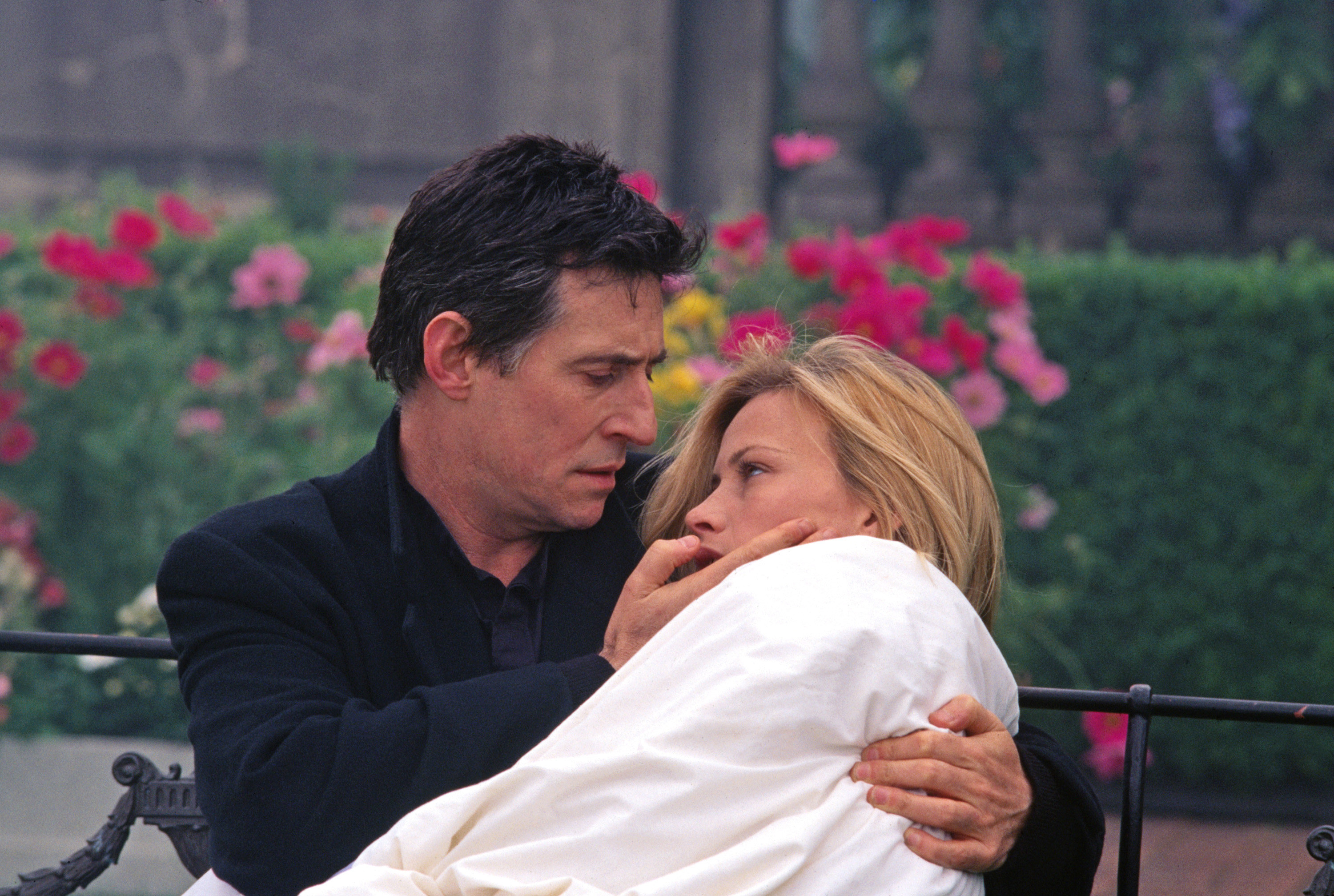 Gabriel Byrne, Patricia Arquette sitting on a bench, her wrapped in a bedsheet