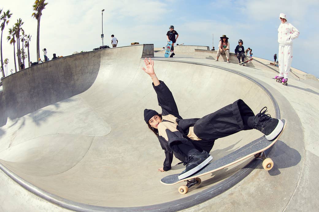 Skater and influencer Brooklinn Khoury in a fish angle lens shot of her doing a trick at the skatepark, with people watching and palm trees