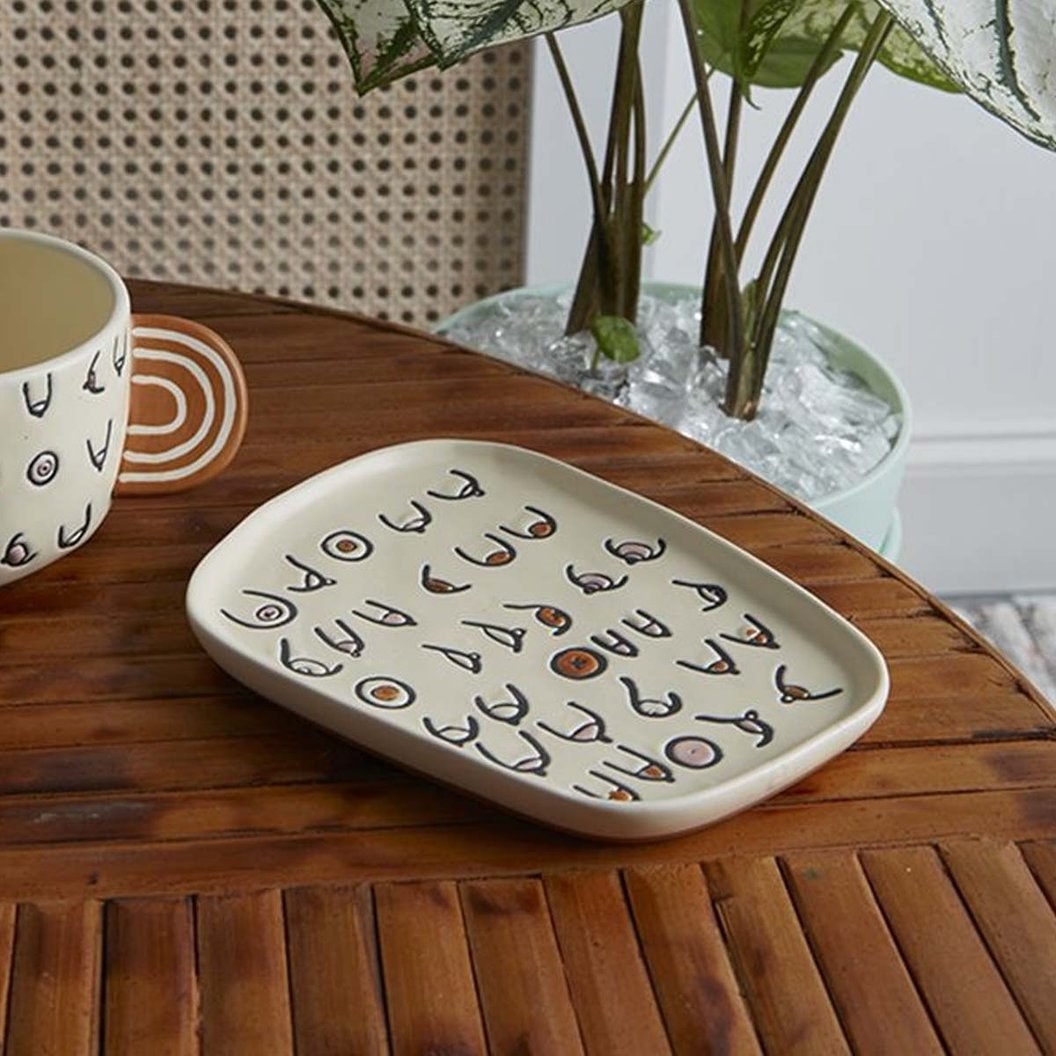 a square catchall tray with hieroglyphics that have boob designs on them