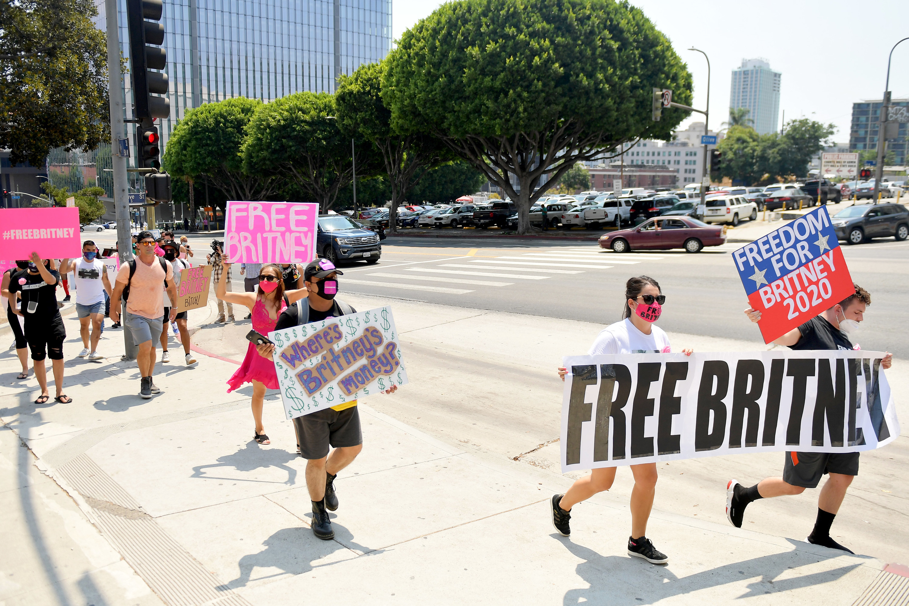 People on a sidewalk wear face masks and carry signs and banners that read &quot;Free Britney,&quot; &quot;Freedom for Britney 2020,&quot; and &quot;Where&#x27;s Britney&#x27;s Money?&quot;