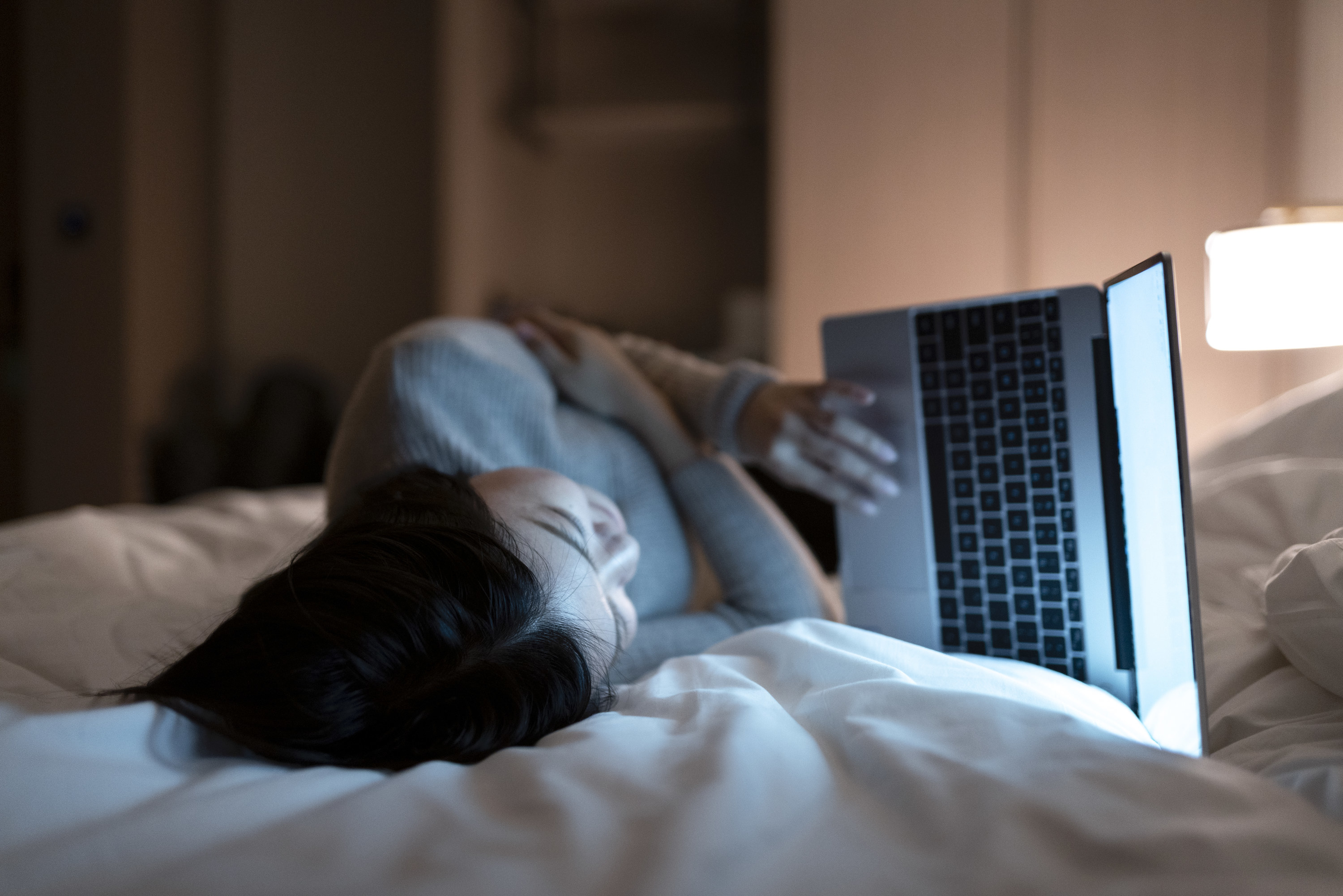 Woman working on her laptop while laying in bed