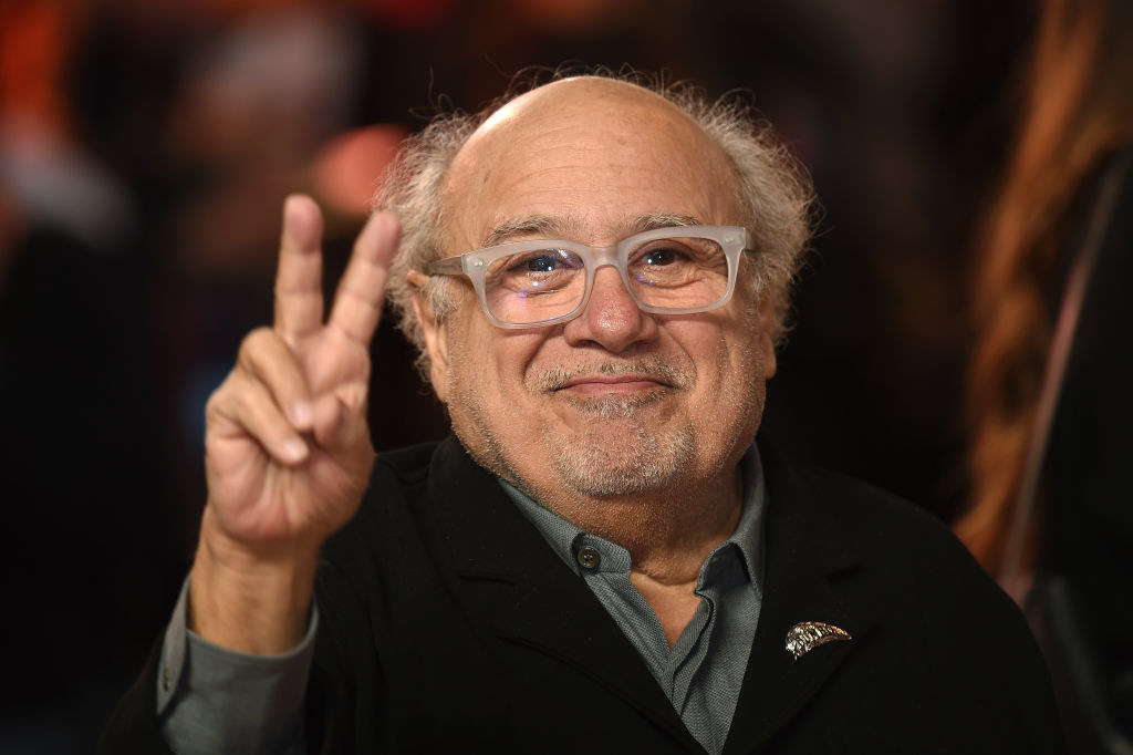 Danny DeVito smiling and giving the V sign