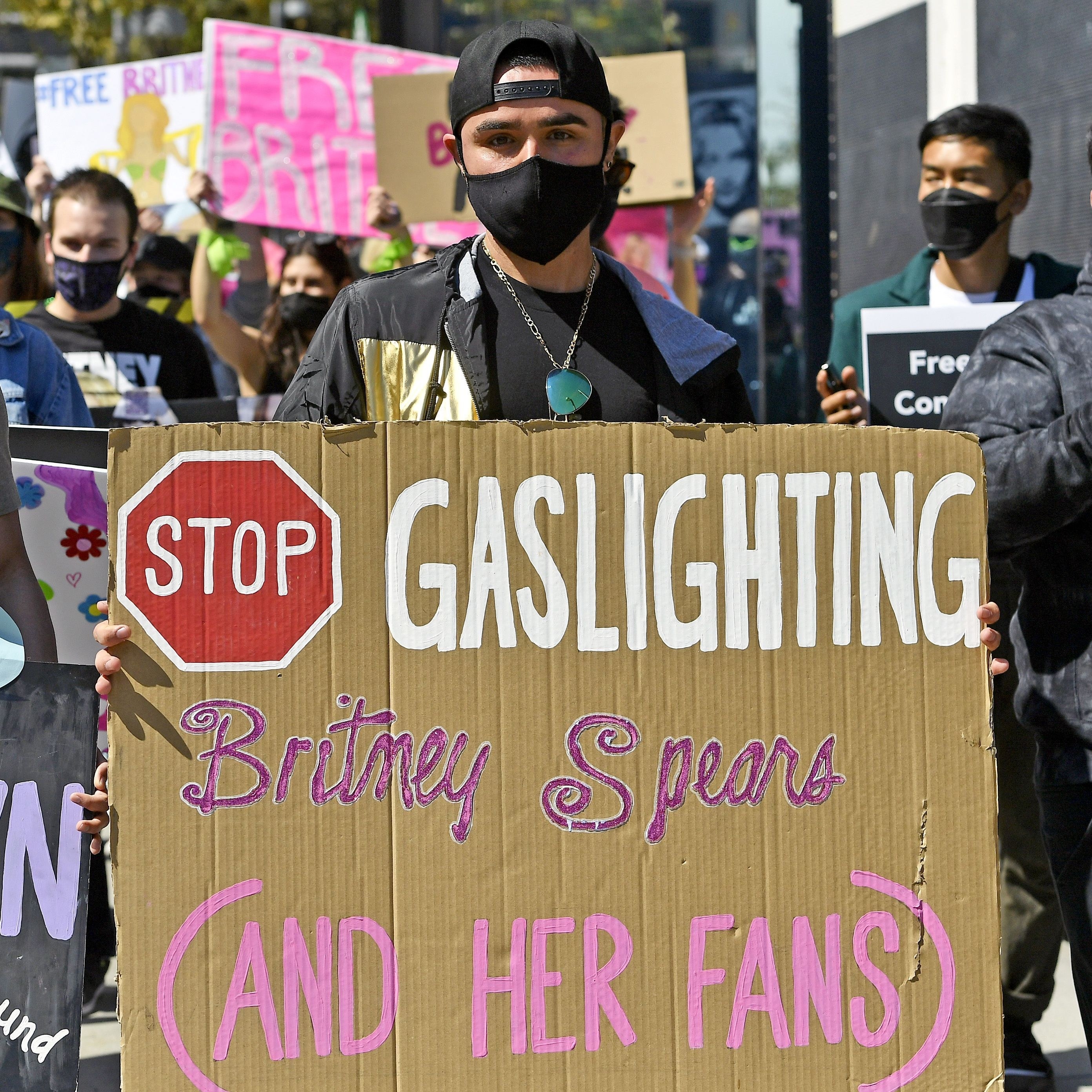 Someone holds a cardboard sign reading &quot;Stop gaslighting Britney Spears and her fans&quot;