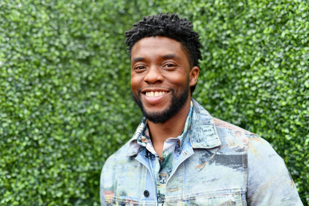 Chadwick Boseman smiling and wearing a denim jacket in front of a background of foliage