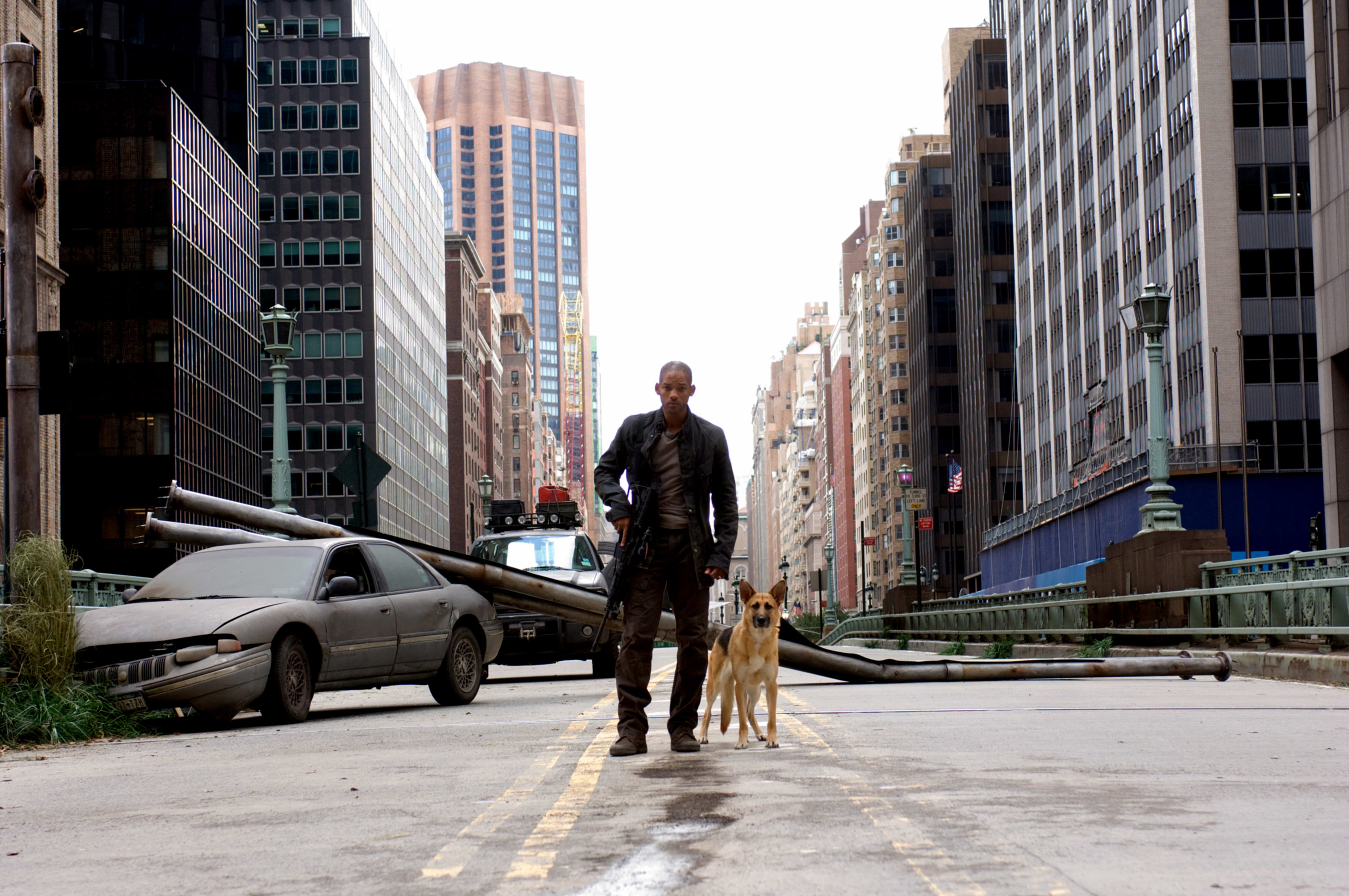 Will Smith as Dr. Robert Neville, in an empty New York street, holding a gun, standing next to his German Shepherd dog