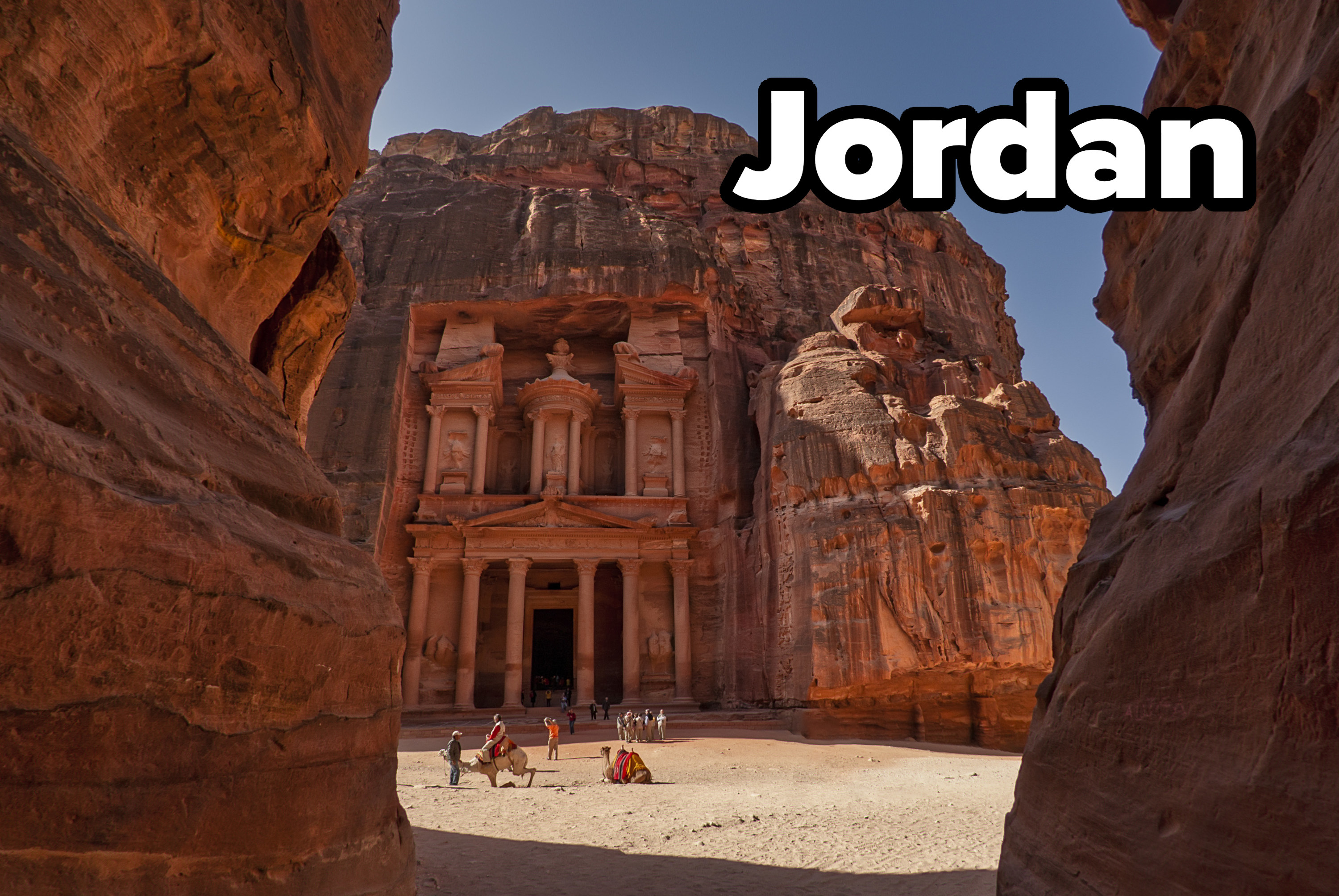 Red stone canyon path leading to Petra&#x27;s treasury in Jordan, with camel sitting in front of the stone structure.