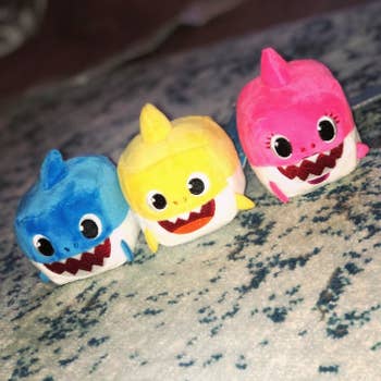 reviewer's photo showing the blue, yellow, and pink shark plush toys