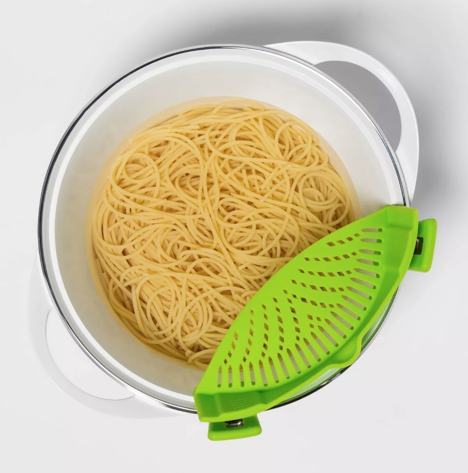 A green clip-on pan strainer attached to a pot of pasta
