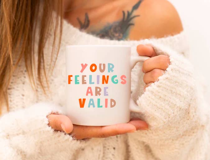 model holding a white mug with multi-colored words that say &quot;your feelings are valid&quot;