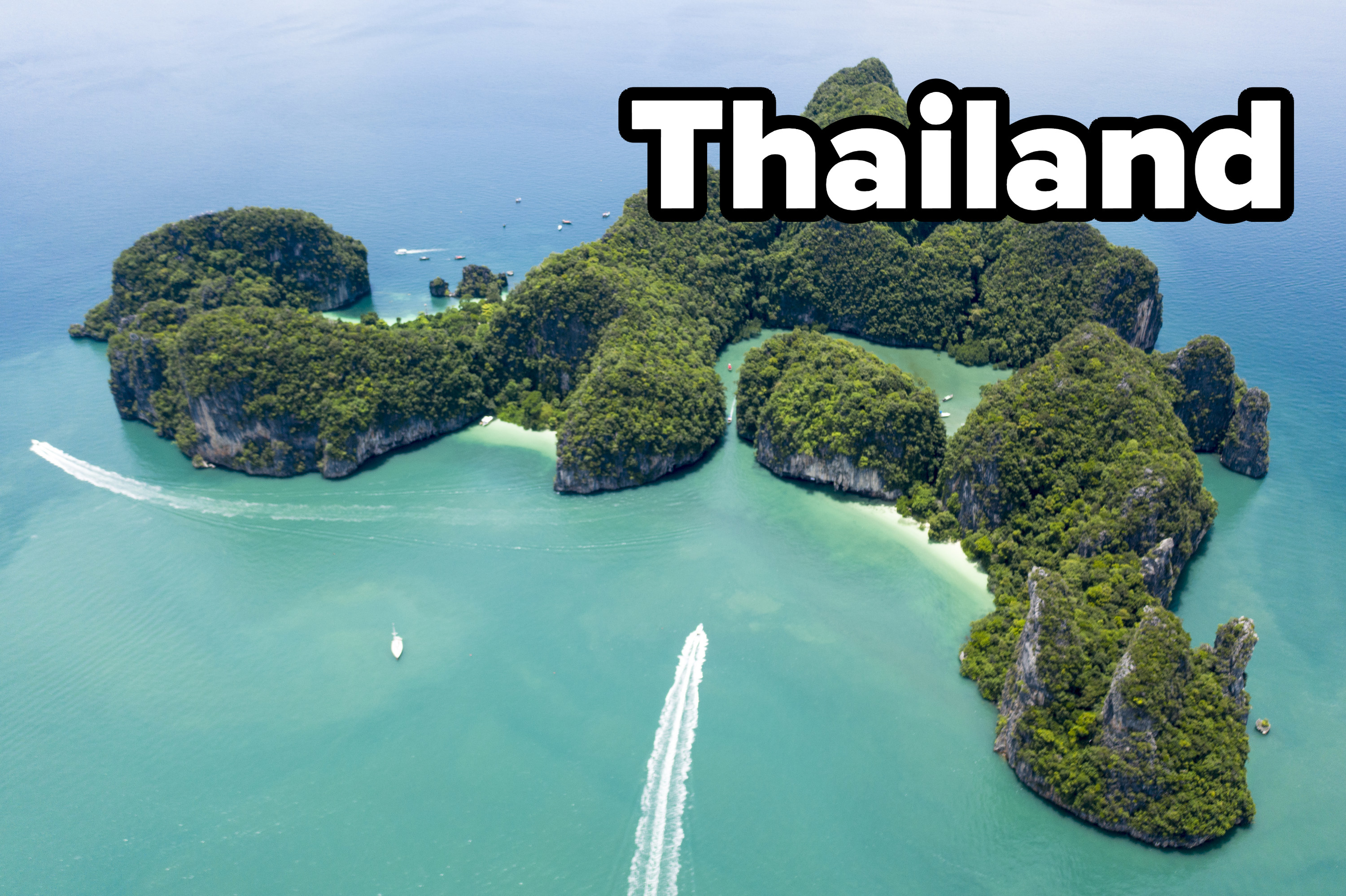 A collection of small island in Thailand with tall tree covered rock formations, white sand beaches, and clear blue ocean waters.