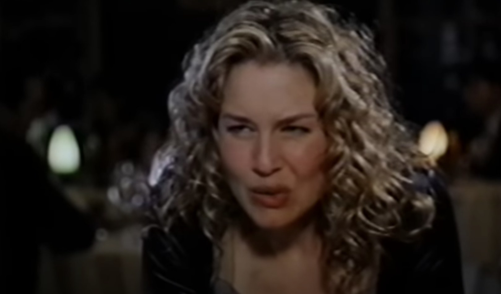 Renée Zellweger has curly blonde hair and she looks at someone off-screen.