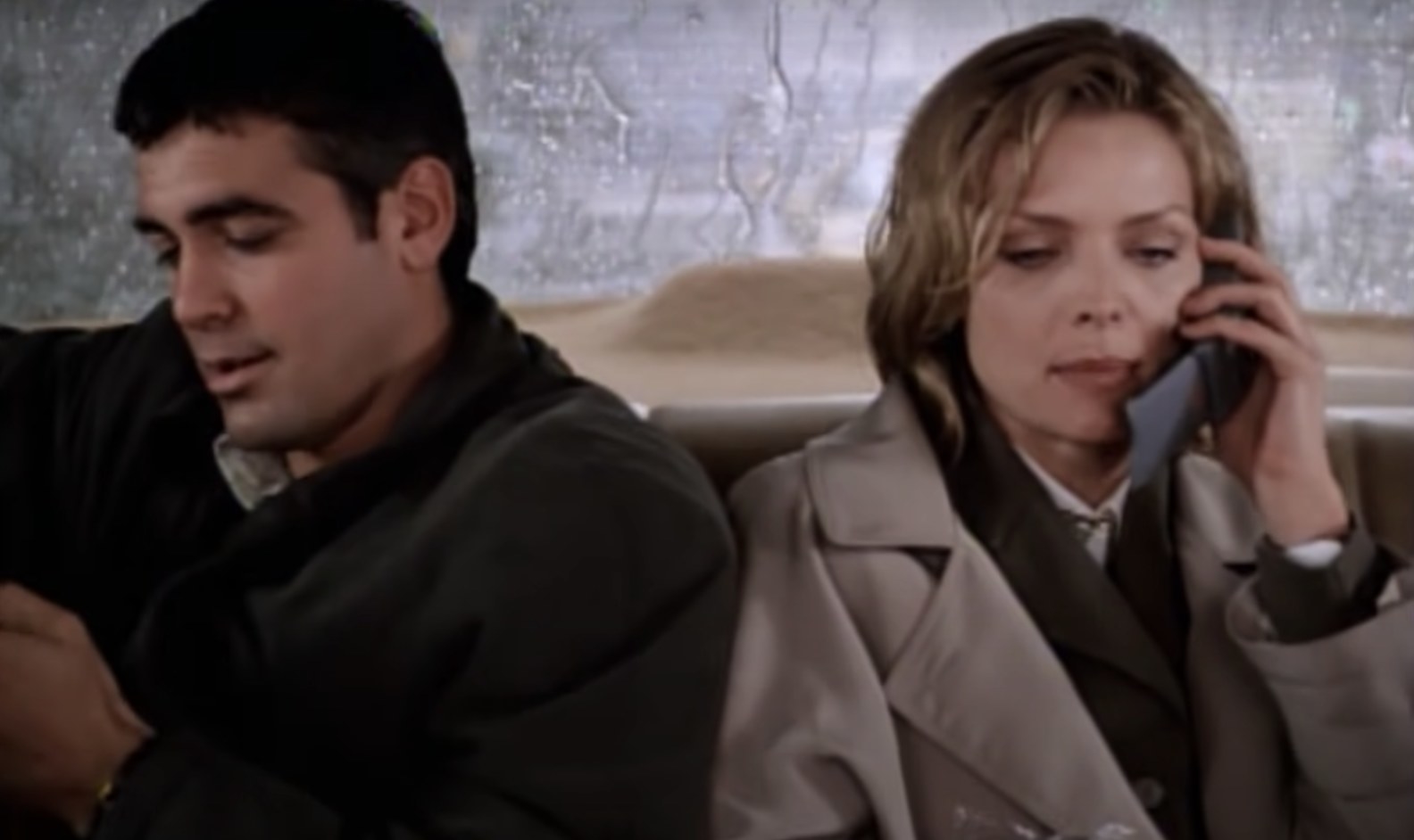 Actors George Clooney sits next to Michelle Pfeiffer in a taxi while she talks on the phone.