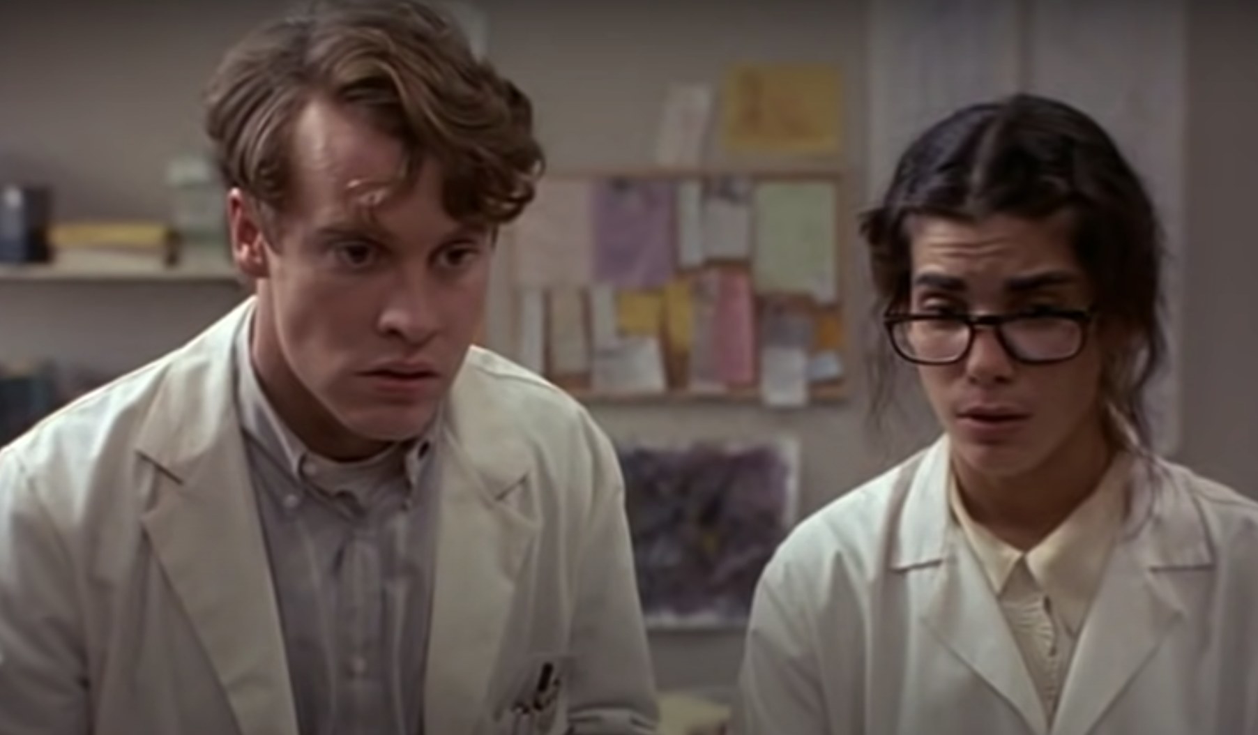 Actors  Tate Donovan and Sandra Bullock wear labcoats while looking distraught.