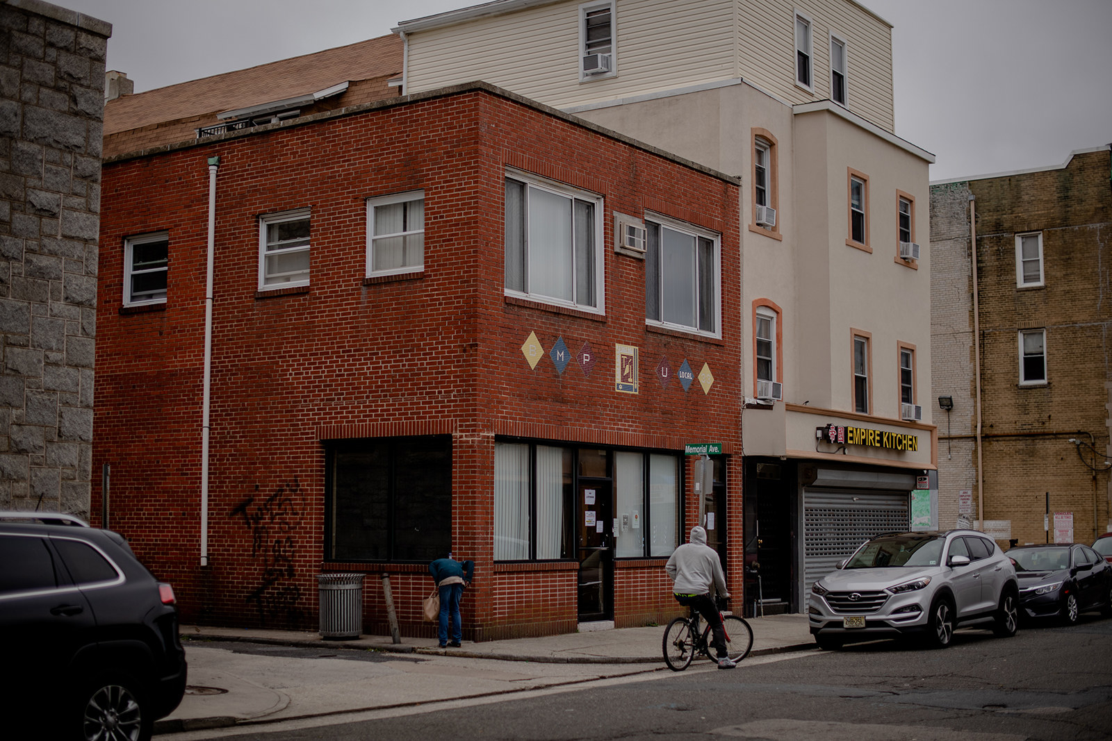 Two buildings on a street with a cyclist and cars parked outside