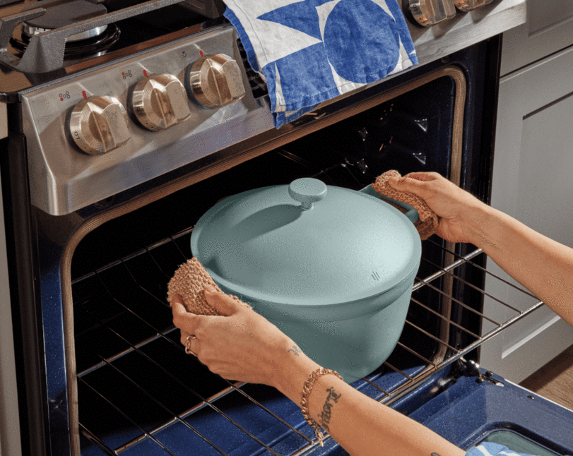 Model is holding the pale blue pot and putting it into the oven