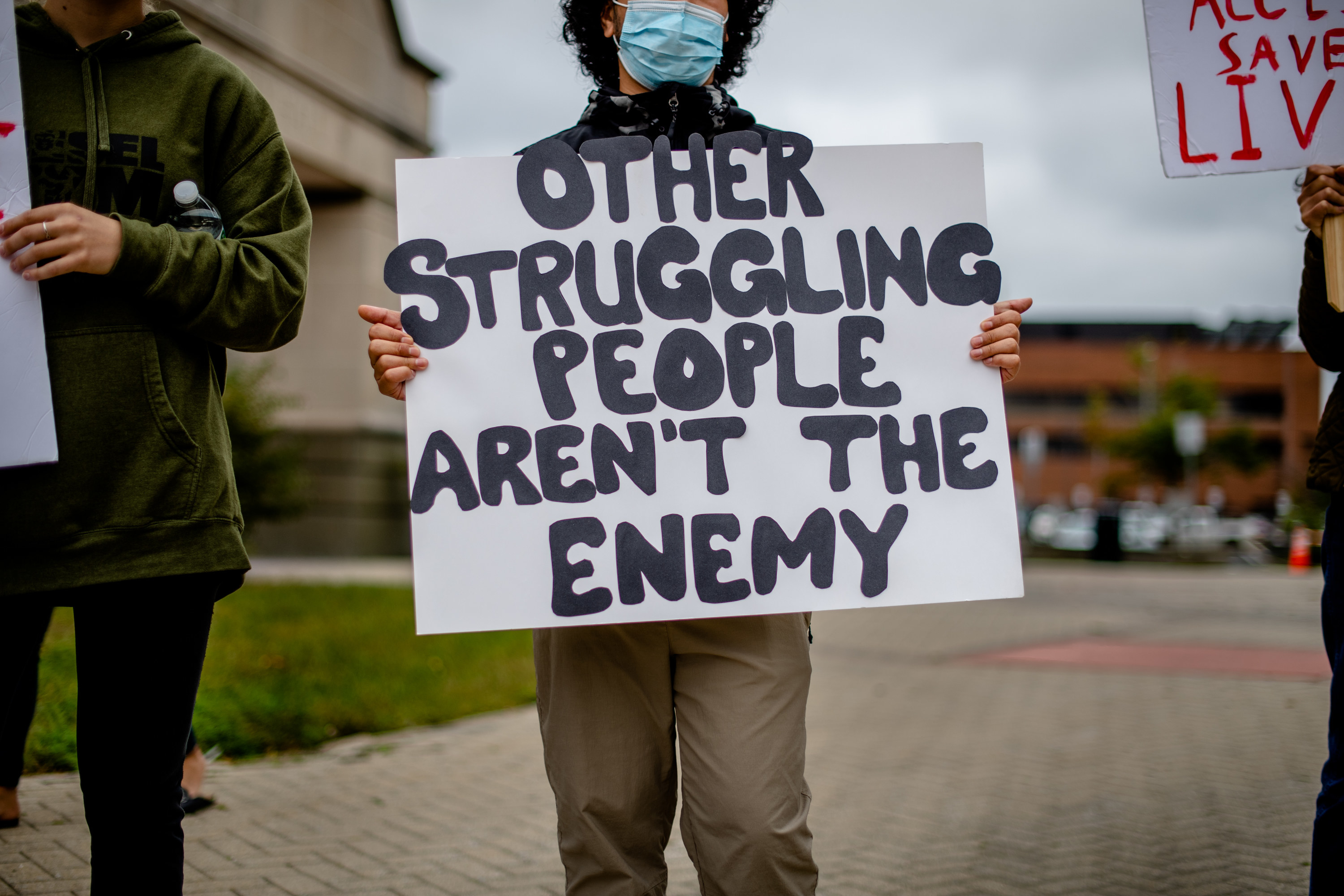 a man holds a sign that reads &quot;other struggling people aren&#x27;t the enemy&quot;
