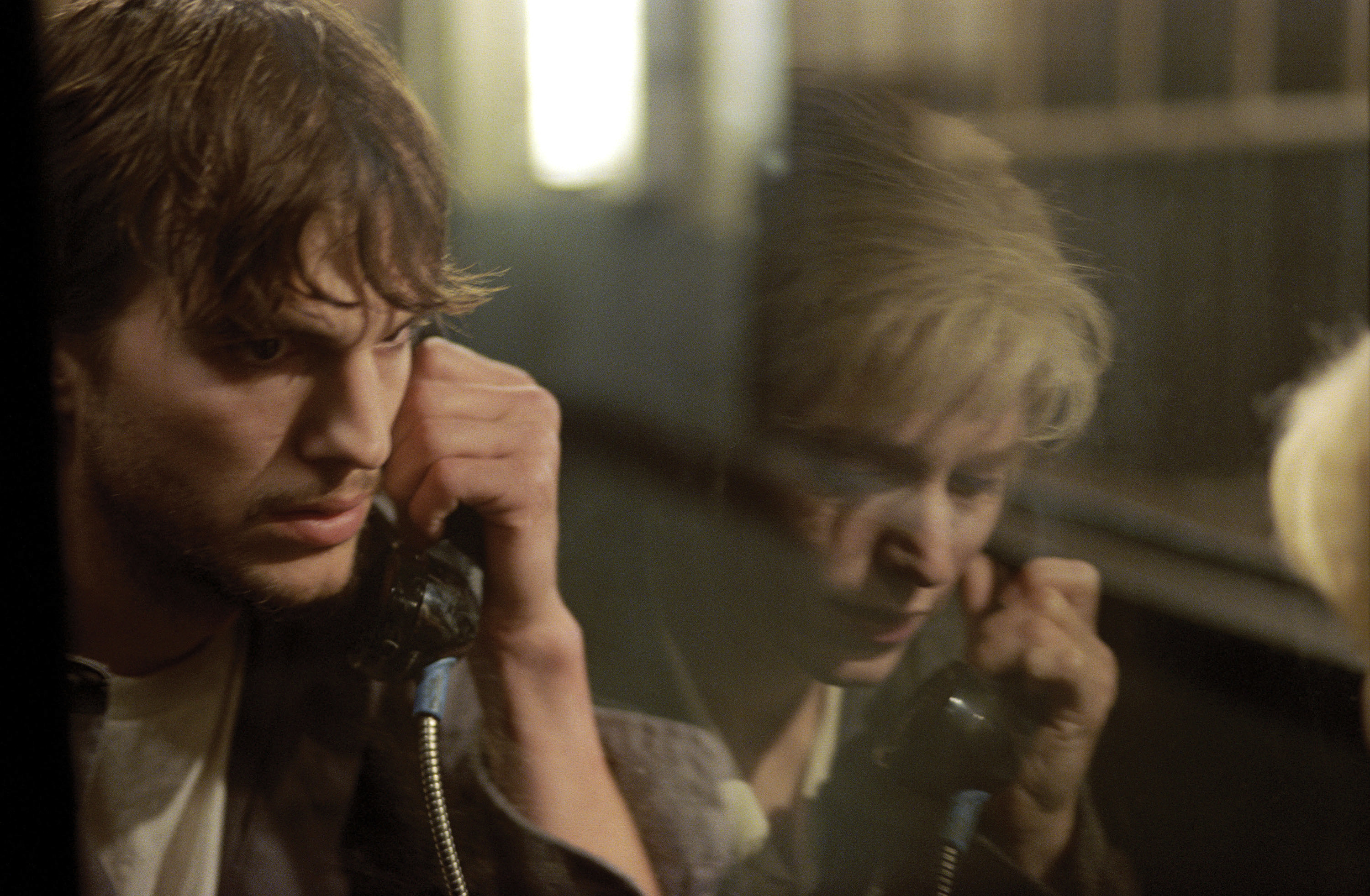 Ashton Kutcher as Evan, talking on a phone with a woman reflected in the glass next to him