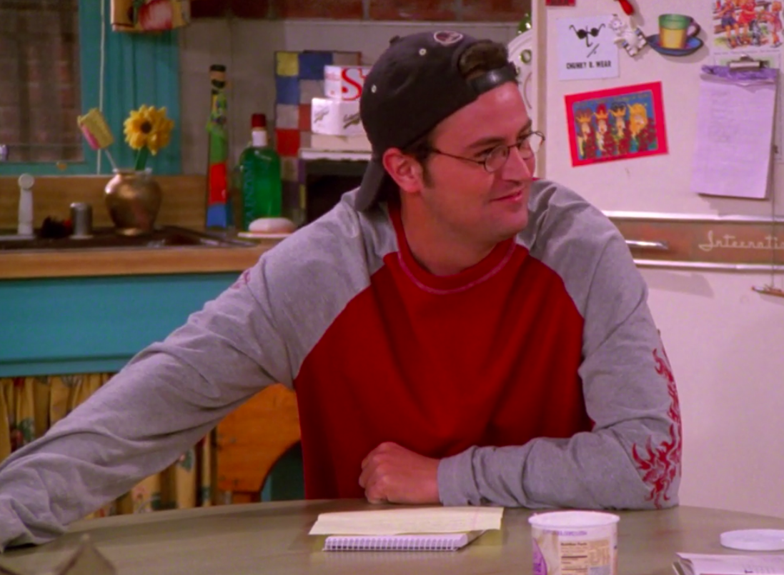 Chandler wearing sneakers, jeans, a shirt with a design on the sleeves, and a backward hat